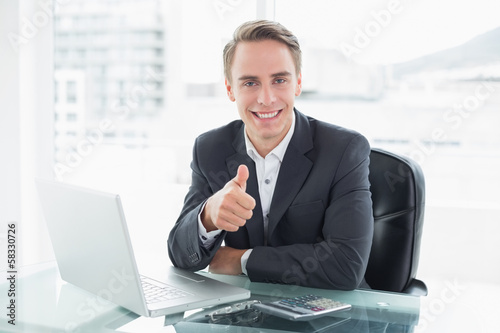 Photo: Businessman with laptop gesturing thumbs up at office desk Businessman with laptop gesturing thumbs up at office desk