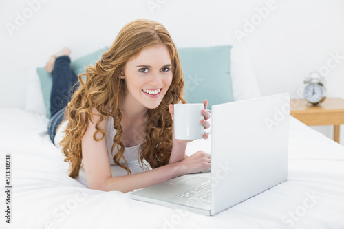 Photo: Casual blond with coffee cup using laptop in bed Casual blond with coffee cup using laptop in bed