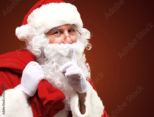 Photo: Santa Claus carrying red sack and showing gesture of silence Santa Claus carrying red sack and showing gesture of silence