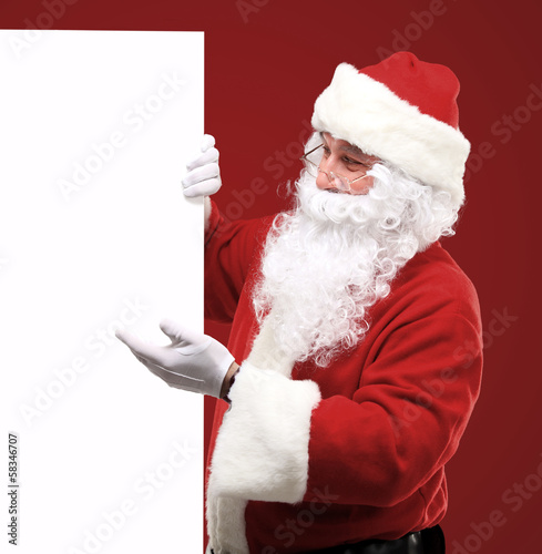 Photo: Santa Claus looking out from behind the blank sign isolated Santa Claus looking out from behind the blank sign isolated