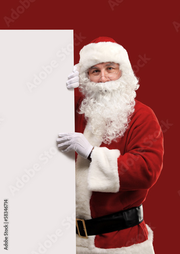 Photo: Santa Claus looking out from behind the blank sign isolated Santa Claus looking out from behind the blank sign isolated