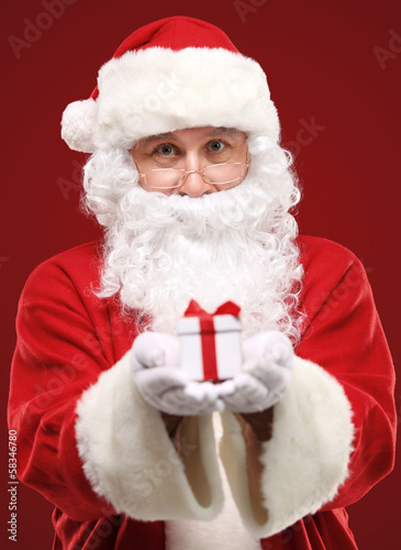 Photo: kind Santa Claus giving xmas present and looking at camera kind Santa Claus giving xmas present and looking at camera