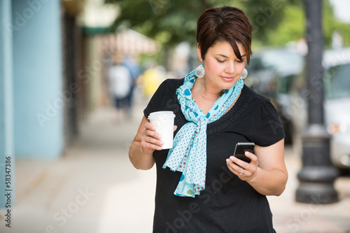 Photo: Woman Holding Coffee Cup While Messaging Through Smartphone Woman Holding Coffee Cup While Messaging Through Smartphone