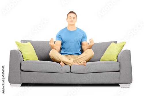 Photo: Young male meditating seated on a sofa Young male meditating seated on a sofa