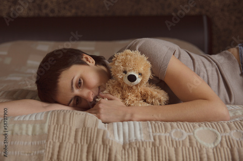 Photo: Young woman lying on the bed with a teddy bear Young woman lying on the bed with a teddy bear
