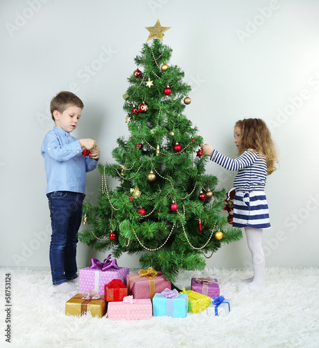 Photo: Kids decorating Christmas tree with baubles in room Kids decorating Christmas tree with baubles in room