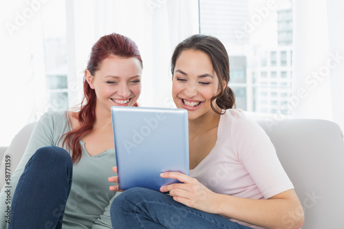 Photo: Cheerful relaxed friends using digital tablet at home Cheerful relaxed friends using digital tablet at home