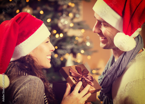 Photo: Christmas Happy Couple with Christmas Gift at Home Christmas Happy Couple with Christmas Gift at Home