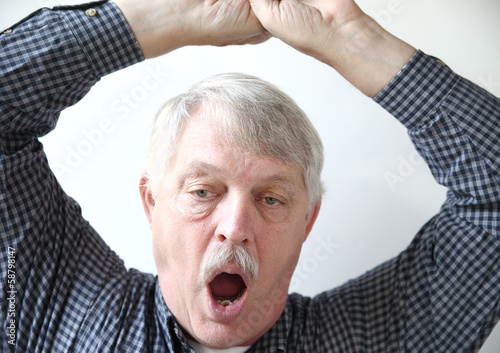 Photo: tired older man stretches and yawns tired older man stretches and yawns