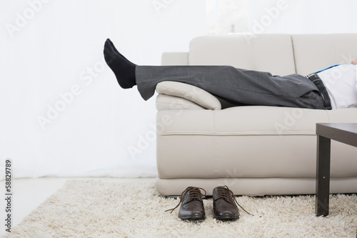 Photo: Low section of a businessman resting on sofa in living room Low section of a businessman resting on sofa in living room
