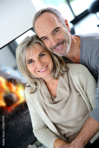 Photo: Cheerful senior couple enjoying fireplace in winter Cheerful senior couple enjoying fireplace in winter