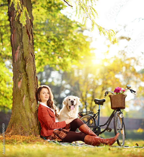 Photo: Pretty female sitting down with her dog in a park Pretty female sitting down with her dog in a park