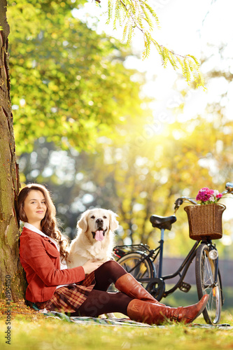 Photo: Pretty female sitting on a grass with her dog and looking at cam Pretty female sitting on a grass with her dog and looking at cam