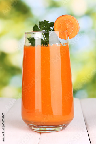 Photo: Glass of carrot juice on wooden table, on green background Glass of carrot juice on wooden table, on green background