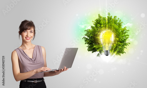 Photo: Young girl presenting idea light bulb with green tree Young girl presenting idea light bulb with green tree
