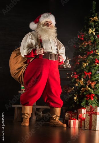 Photo: Real Santa Claus carrying big bag full of gifts, at home near Ch Real Santa Claus carrying big bag full of gifts, at home near Ch