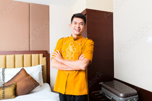 Photo: Asian Chinese porter bringing suitcase to luxury hotel room Asian Chinese porter bringing suitcase to luxury hotel room
