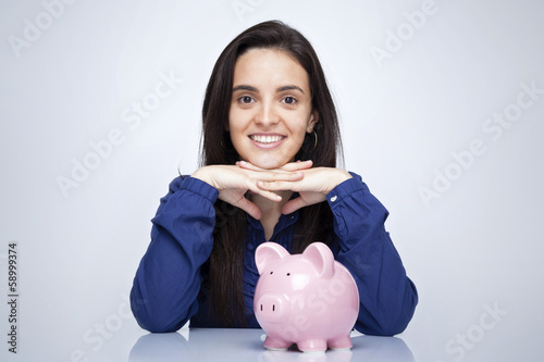 Photo: Happy smiling woman and a piggy bank against gray background Happy smiling woman and a piggy bank against gray background