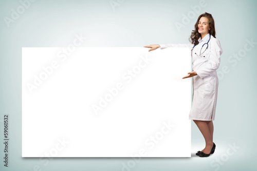 Photo: young woman doctor standing near a blank banner young woman doctor standing near a blank banner