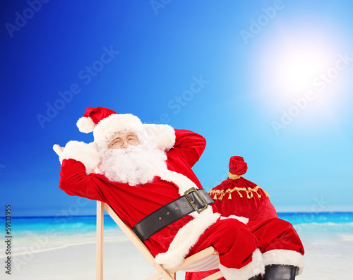 Photo: Santa Claus sitting on a chair and relaxing, on a beach Santa Claus sitting on a chair and relaxing, on a beach