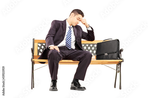 Photo: Worried young businessperson sitting on a wooden bench Worried young businessperson sitting on a wooden bench