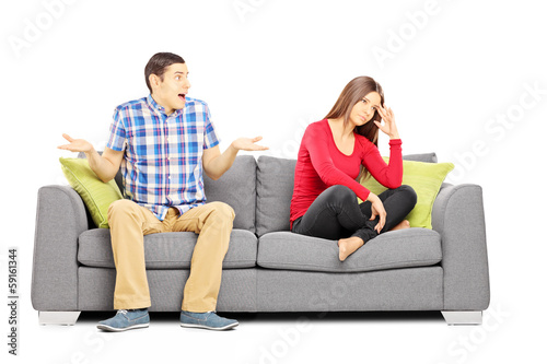 Photo: Young heterosexual couple sitting on a couch during an argument Young heterosexual couple sitting on a couch during an argument