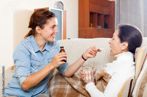 Photo: Adult daughter giving the liquid medicament to mother Adult daughter giving the liquid medicament to mother