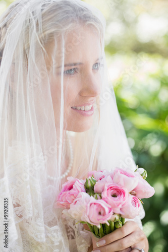 Photo: Happy bride wearing veil over face holding rose bouquet Happy bride wearing veil over face holding rose bouquet