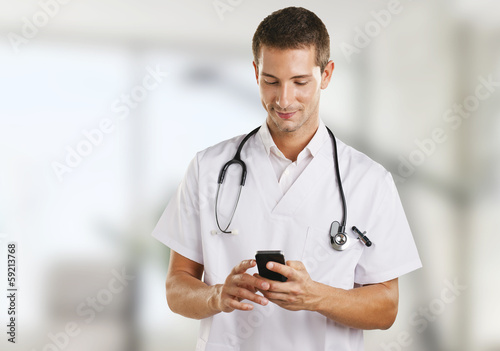 Photo: Doctor man with stethoscope sending a message in the hospital. Doctor man with stethoscope sending a message in the hospital.