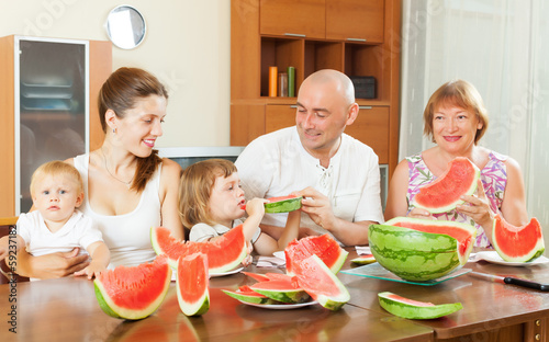 Photo: happy three generations family eating melon happy three generations family eating melon