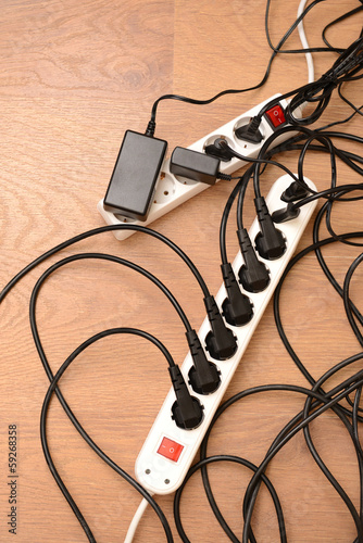 Photo: Overloaded power boards, on wooden floor background Overloaded power boards, on wooden floor background
