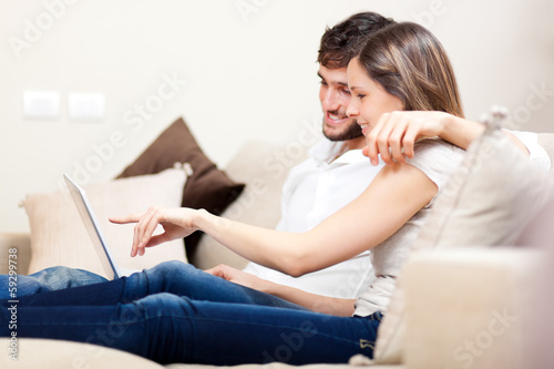 Photo: In love couple using a tablet computer in their living room In love couple using a tablet computer in their living room