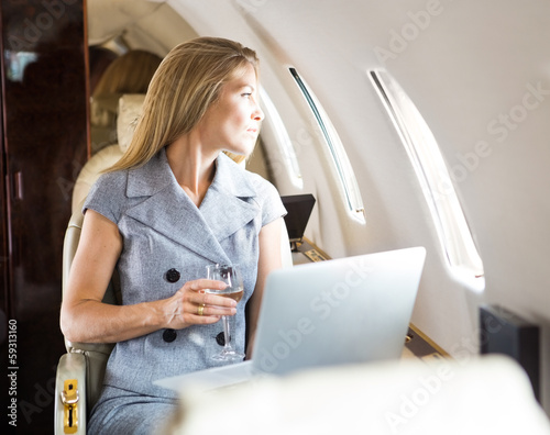 Photo: Businesswoman Looking Through Window Of Private Jet Businesswoman Looking Through Window Of Private Jet