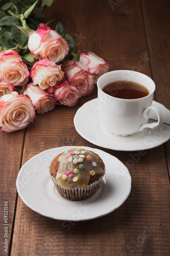 Photo: Tasty muffin and a cup of hot tea with roses on wooden table Tasty muffin and a cup of hot tea with roses on wooden table