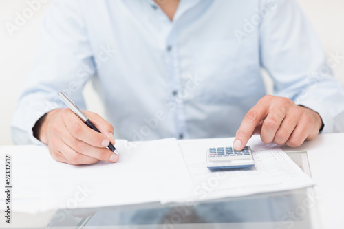 Photo: Mid section of a young man with bills and calculator Mid section of a young man with bills and calculator