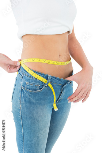 Photo: Mid section of a woman measuring waist in a big sized jeans Mid section of a woman measuring waist in a big sized jeans
