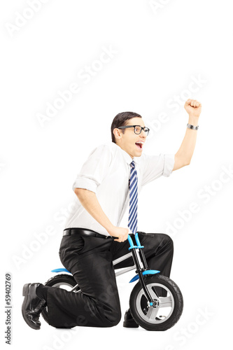 Photo: Excited young businessperson riding a small bicycle gesturing Excited young businessperson riding a small bicycle gesturing