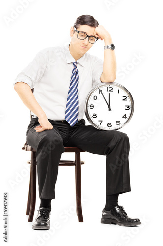 Photo: Sad male sitting on a wooden chair and holding a clock Sad male sitting on a wooden chair and holding a clock