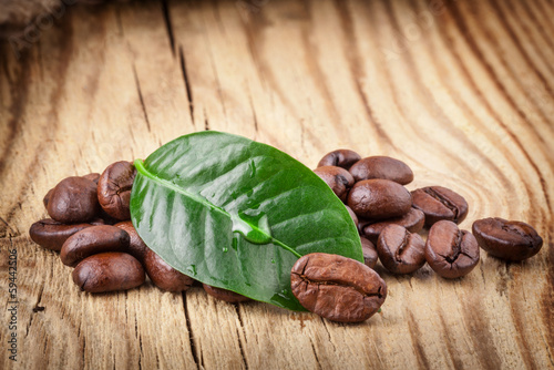 Photo: Coffee grains and green leaf on wooden background Coffee grains and green leaf on wooden background