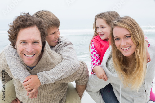 Photo: Happy couple piggybacking kids at beach Happy couple piggybacking kids at beach