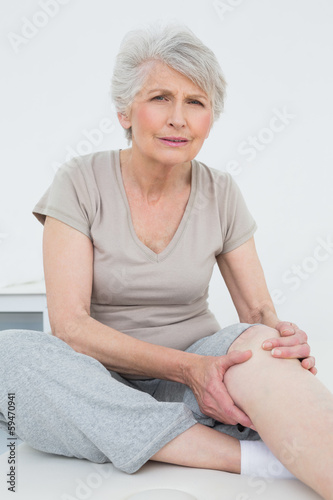 Photo: Senior woman with painful knee sitting on examination table Senior woman with painful knee sitting on examination table