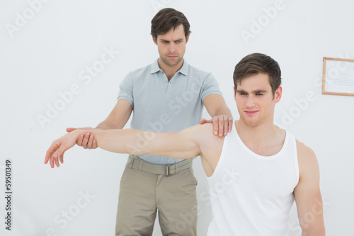Photo: Male physiotherapist examining a young mans arm Male physiotherapist examining a young mans arm