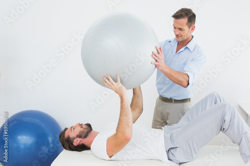 Photo: Physical therapist assisting man with yoga ball Physical therapist assisting man with yoga ball