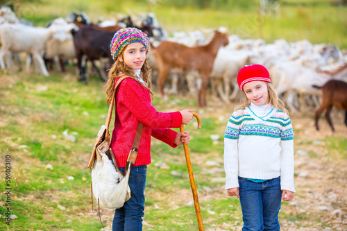 Photo: Kid girl shepherdess sisters happy with flock of sheep and stick Kid girl shepherdess sisters happy with flock of sheep and stick