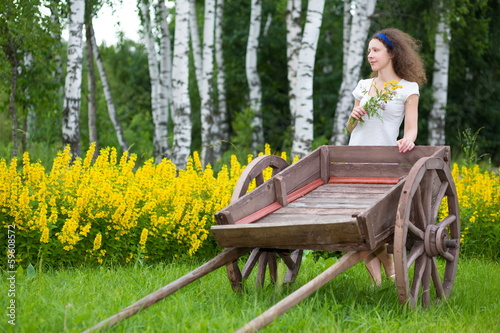Photo: Young girl with old wooden cart on the field with green grass Young girl with old wooden cart on the field with green grass