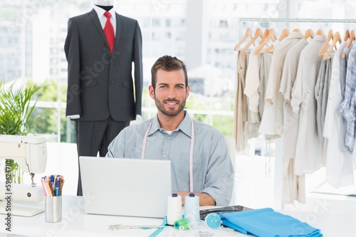 Photo: Smiling male fashion designer using laptop in studio Smiling male fashion designer using laptop in studio