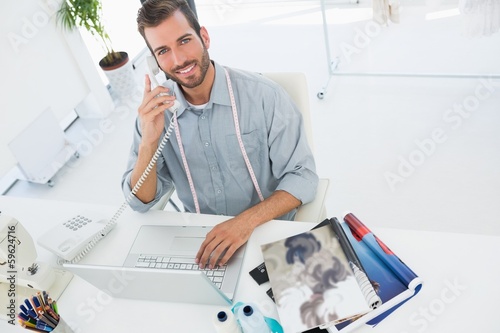 Photo: Fashion designer using laptop and phone in studio Fashion designer using laptop and phone in studio