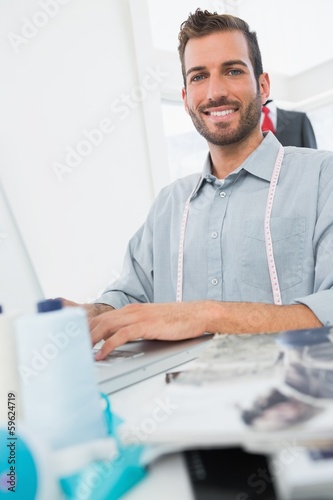 Photo: Smiling young male fashion designer using laptop Smiling young male fashion designer using laptop