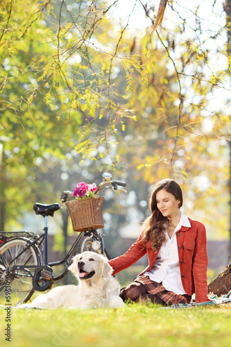 Photo: Beautiful female sitting on a grass with her dog in a park Beautiful female sitting on a grass with her dog in a park