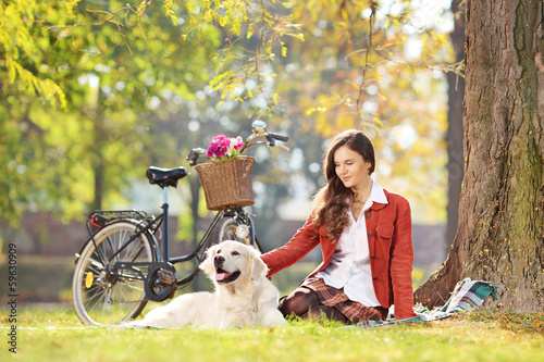 Photo: Beautiful female sitting on a grass with her dog in a park Beautiful female sitting on a grass with her dog in a park